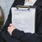 Close-up of a person holding a home insurance policy on a clipboard, captured indoors.